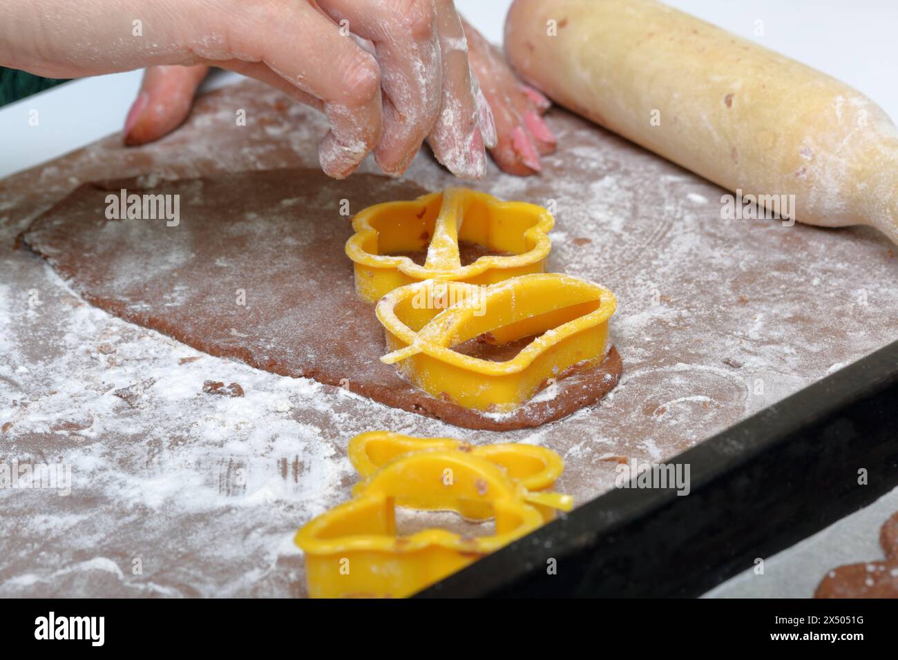 Une femme forme un pain d'épices en utilisant un moule en plastique sur une pâte roulée. La surface de travail est en farine, les outils se trouvent à côté. Cuisson du pain d'épices. Banque D'Images