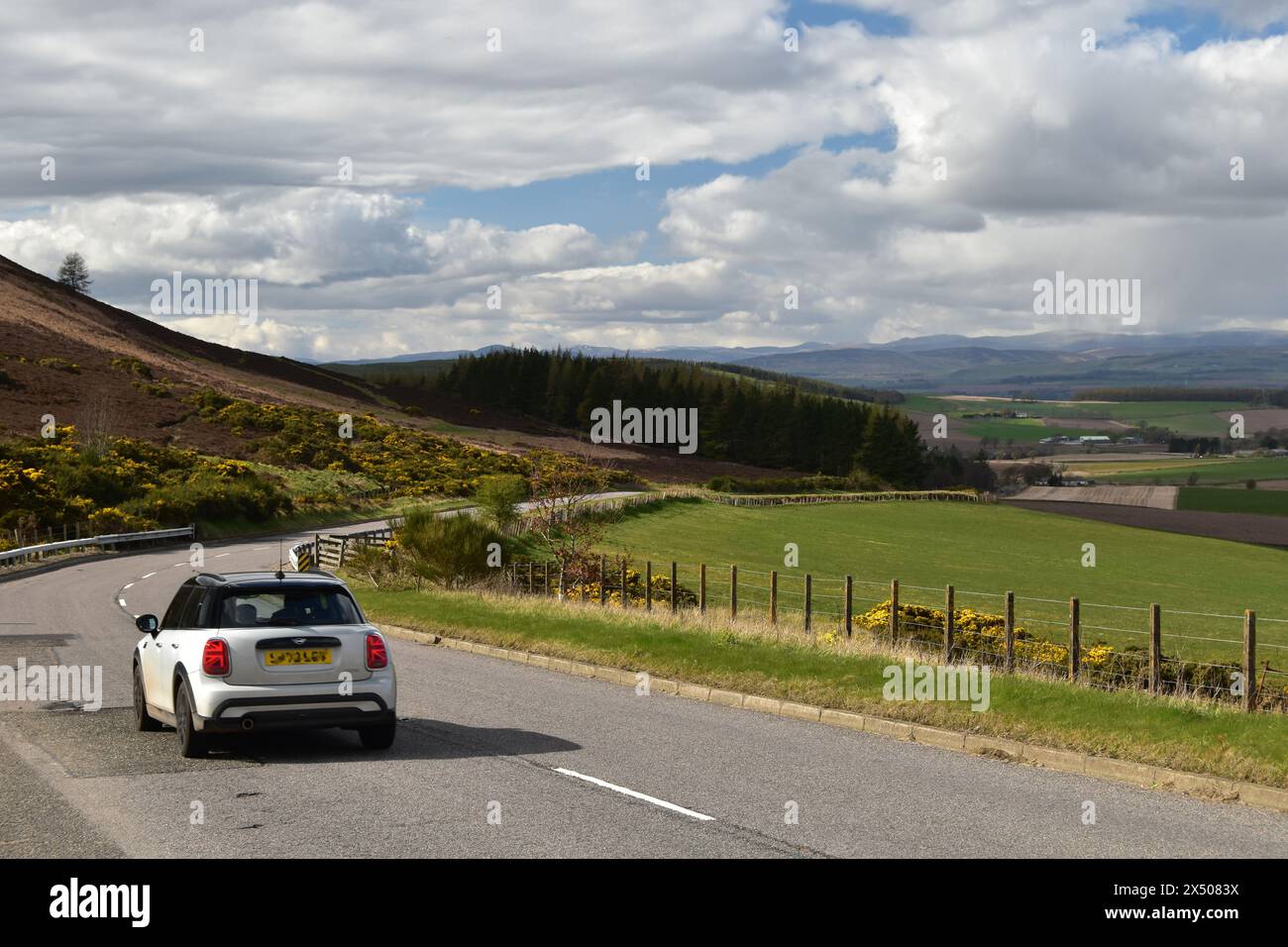 Une voiture blanche conduite le long de l'A928 en direction de Glamis, devant un point de vue de la vallée de Strathmore à Angus, en Écosse, par un jour de printemps brillant. Banque D'Images