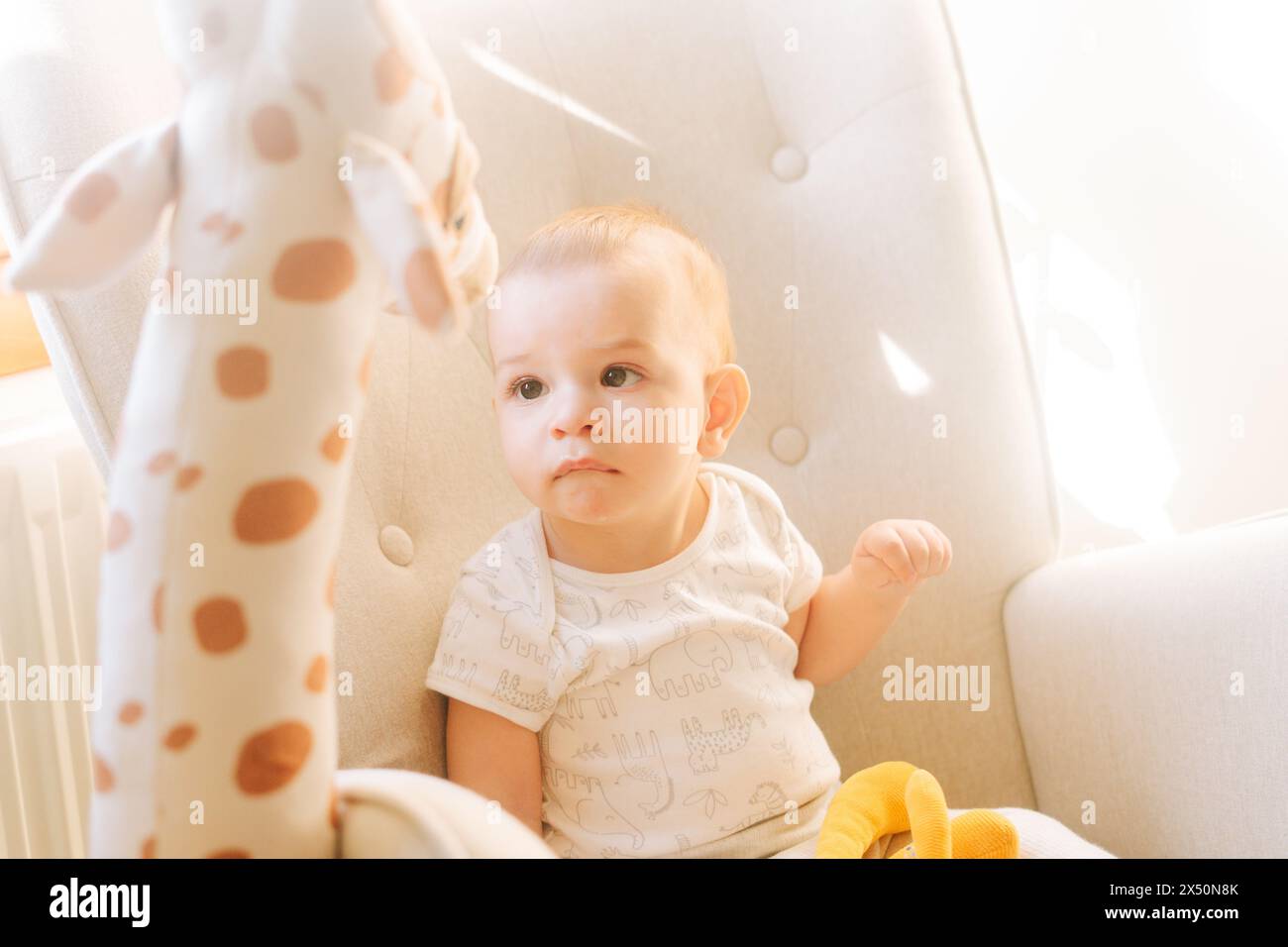 Portrait d'un bébé de neuf mois avec une girafe en peluche assise dans une chaise à bascule Banque D'Images
