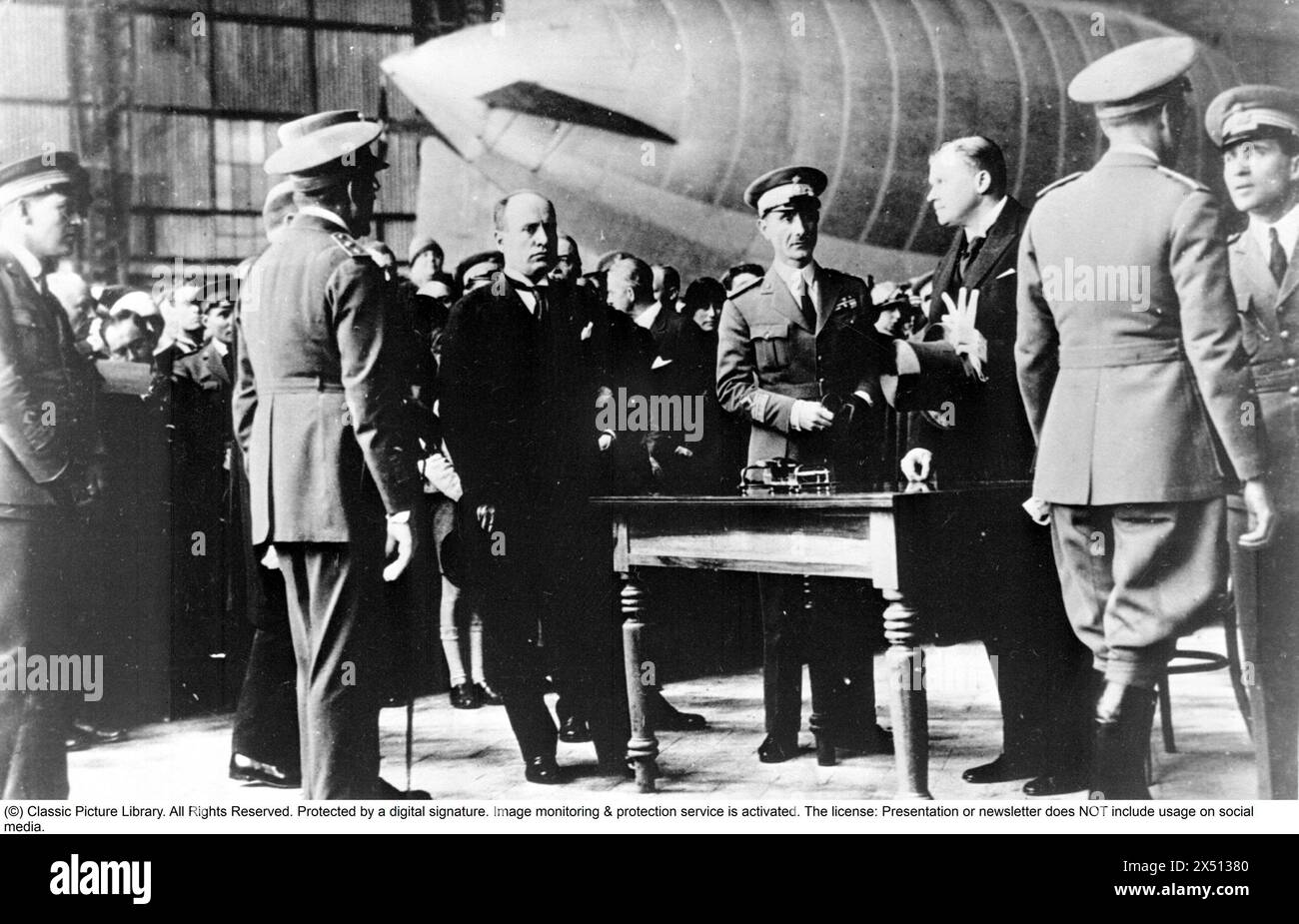 Roald Amundsen. Explorateur polaire norvégien. 1872-1928. Sur la photo : la cérémonie de prise de contrôle du dirigeable 'Norge' dans le hall du dirigeable à l'aéroport de Ciampino. Rolf Thommessen de la Luftseiladsforeningen et Benito Mussolini ainsi que plusieurs officiers italiens se tiennent autour de la table où le contrat a été signé. Le dirigeable en arrière-plan était beaucoup plus petit que 'Norge'. 29 mars 1926. Banque D'Images