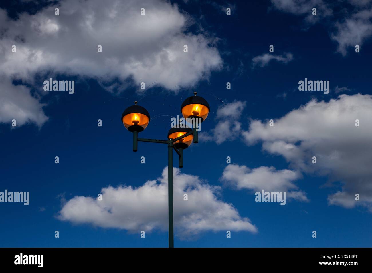 Lumières allumées à la lumière du jour. Ciel de nuages bleu et blanc dramatique avec des lumières luisantes jaunes allumées , en plein jour . L'éclairage en sodium à dôme rond crée de la chaleur Banque D'Images