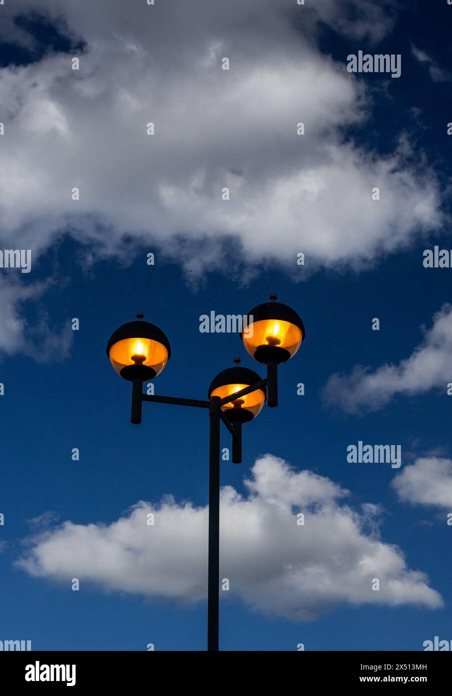 Lumières allumées à la lumière du jour. Ciel de nuages bleu et blanc dramatique avec des lumières luisantes jaunes allumées , en plein jour . L'éclairage en sodium à dôme rond crée de la chaleur Banque D'Images