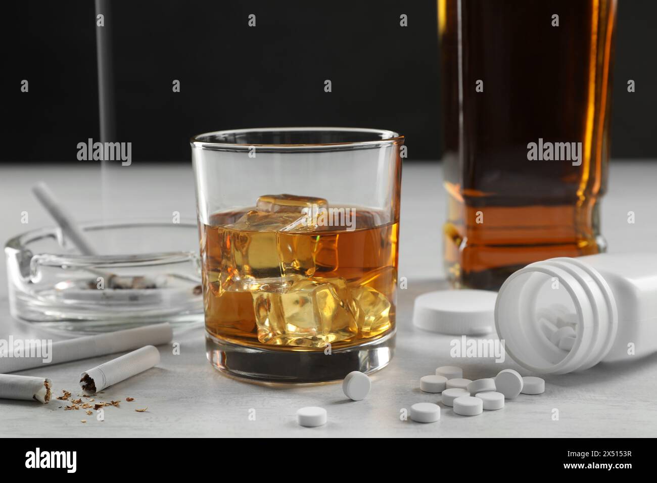 Alcoolisme et toxicomanie. Whisky en verre, cigarettes et pilules sur table blanche Banque D'Images
