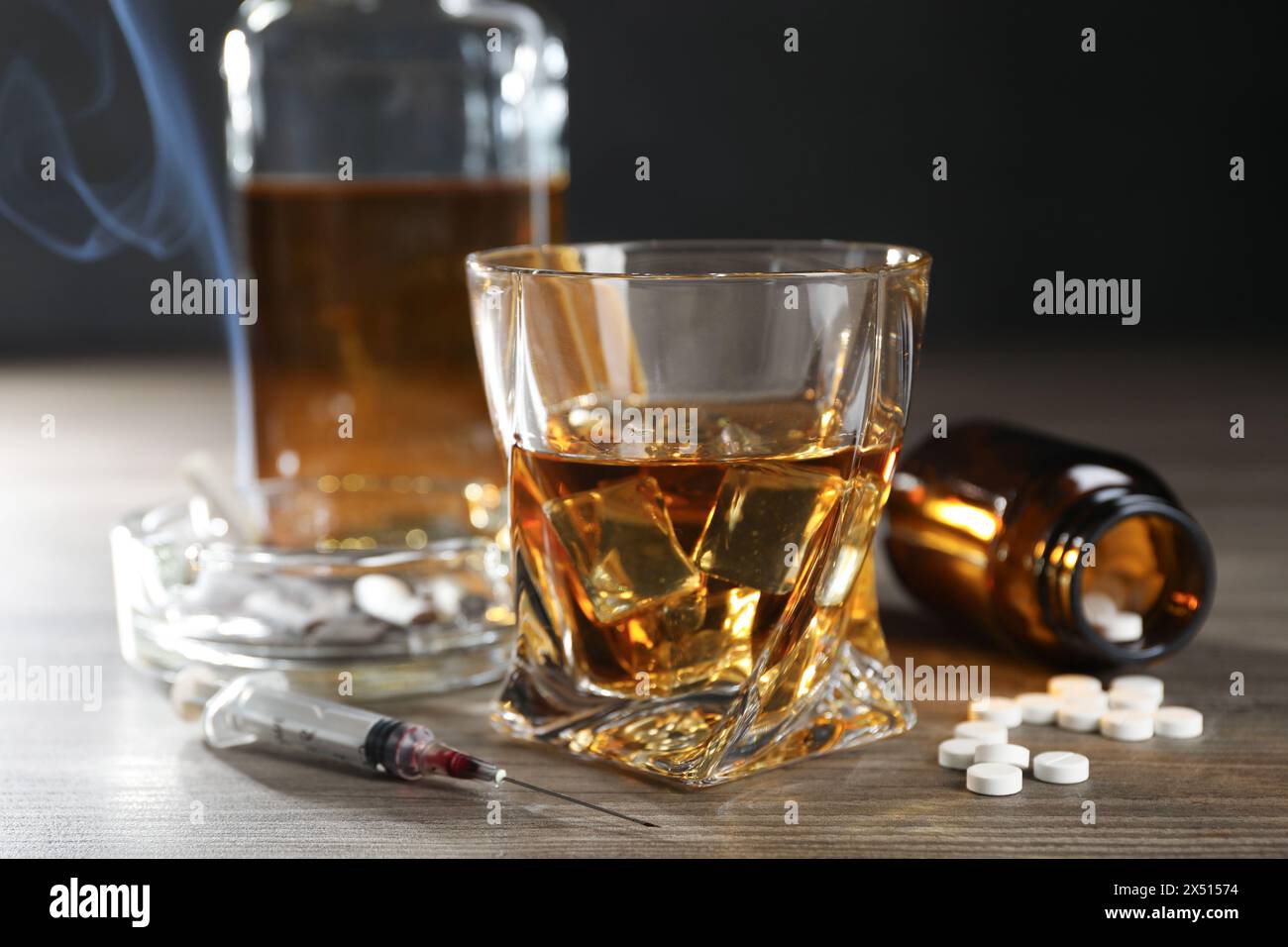Alcoolisme et toxicomanie. Whisky en verre, seringue, pilules et cigarettes sur table en bois Banque D'Images