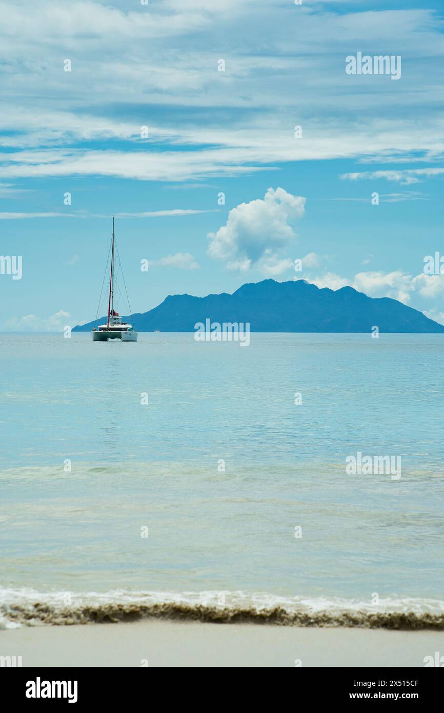 Yacht amarrage près de la belle plage de vallon, mer calme, île silhouette à l'arrière. Mahé, Seychelles Banque D'Images