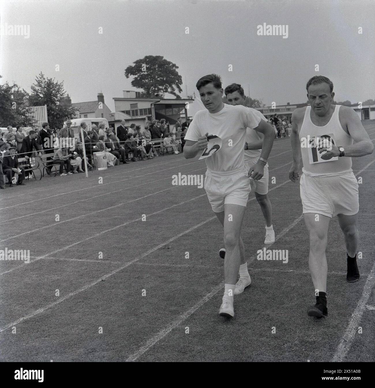 Années 1960, historique, à l'extérieur sur une piste d'herbe athlètes masculins concourant dans une course de marche à une journée sportive Combined services. Les marcheurs de course doivent maintenir un contact continu du pied avec le sol, avec la jambe de soutien droite lorsqu'ils font le tour de la piste. Le sport est également connu sous le nom de course talon-orteils. Banque D'Images