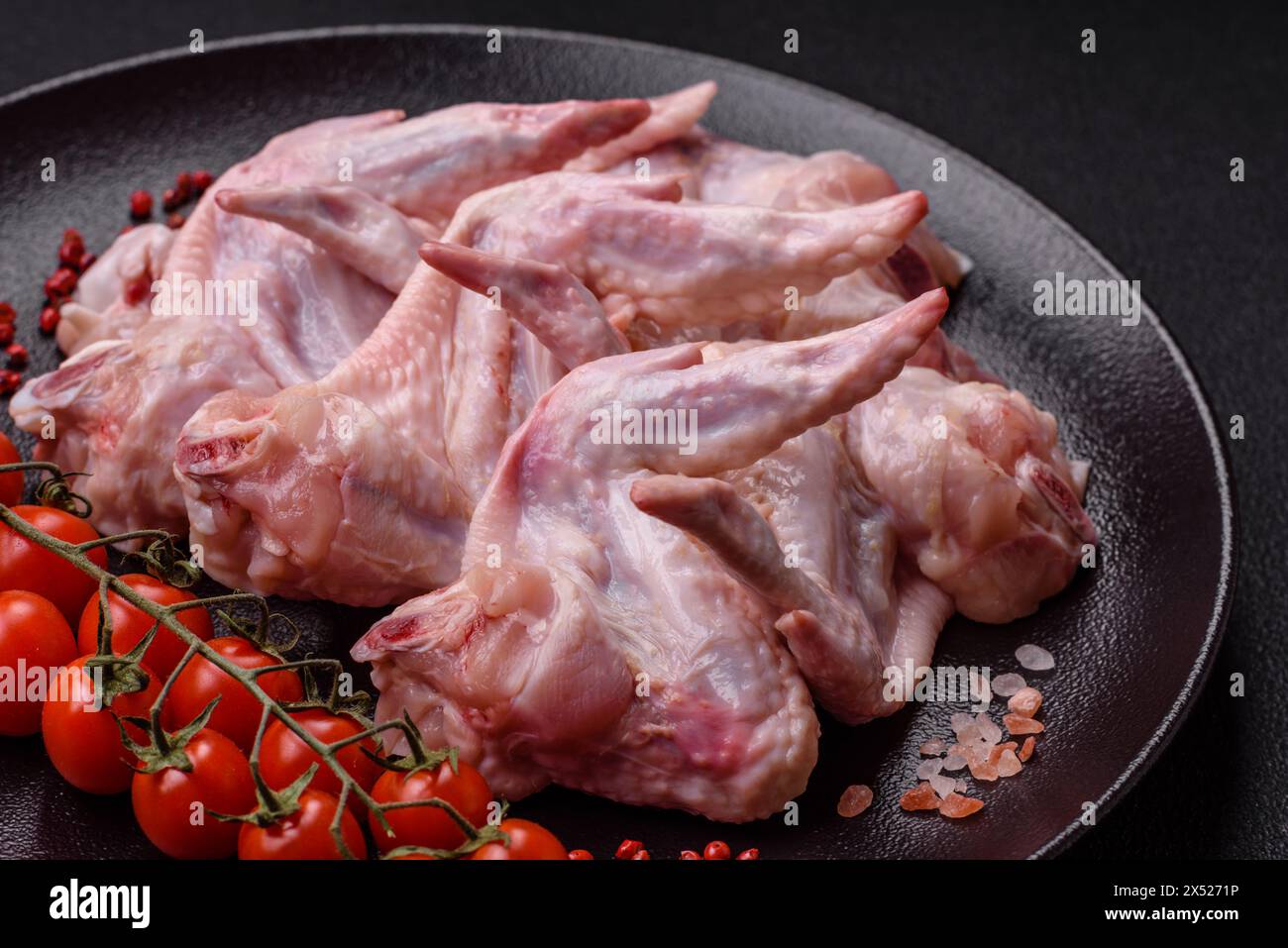 Ailes de poulet fraîches avec du sel, des épices et des herbes sur un fond de béton foncé Banque D'Images