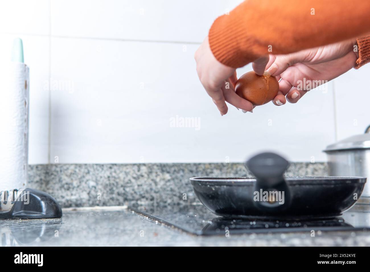 mains ouvrant un œuf pour le faire frire sur une poêle dans la cuisine Banque D'Images