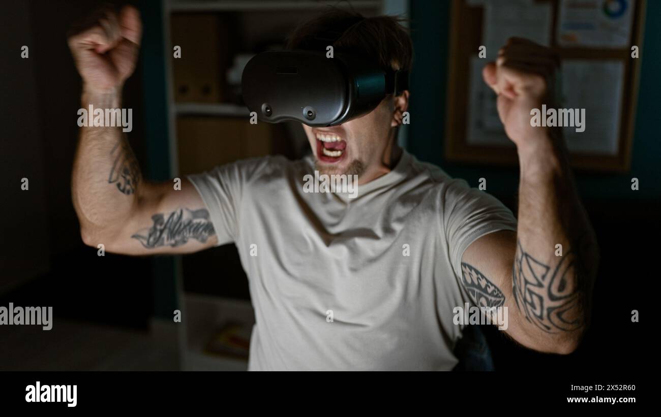 Un jeune homme caucasien avec une barbe et des tatouages célèbre triomphalement tout en utilisant un casque vr à l'intérieur. Banque D'Images