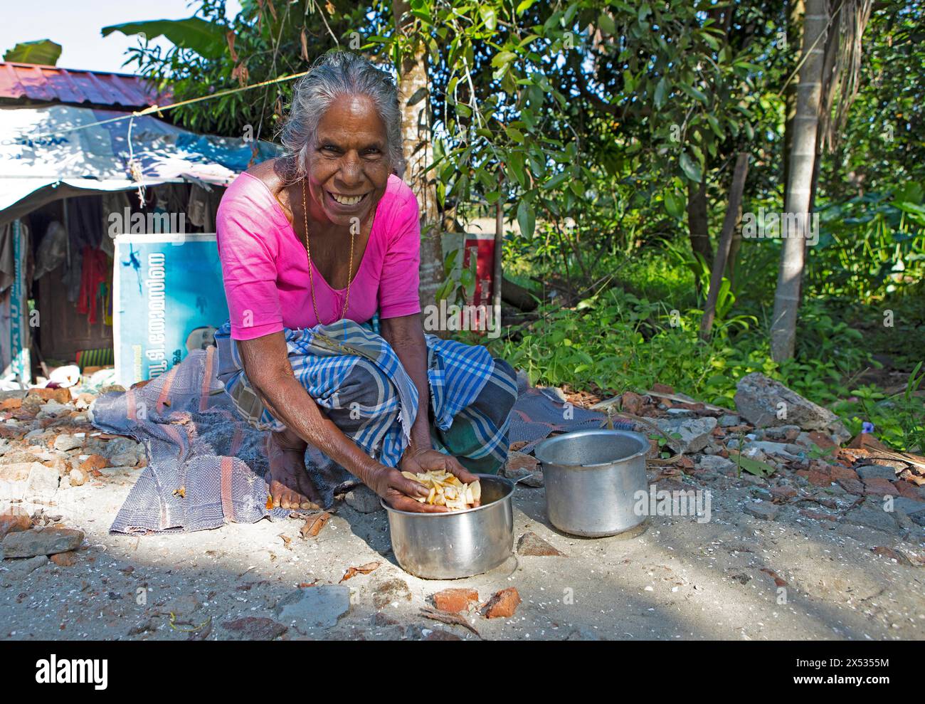 Femme indienne, 78 ans, accroupie au sol et lave les racines de manioc, Kavanattinkara, Backwaters, Kerala, Inde Banque D'Images