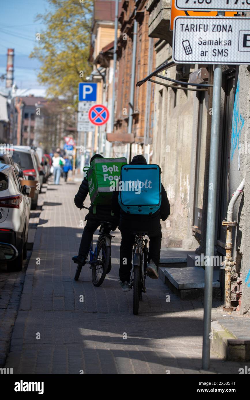 Deux coursiers à vélo avec des sacs à dos de livraison roulent dans une rue de la ville, Riga, Lettonie Banque D'Images