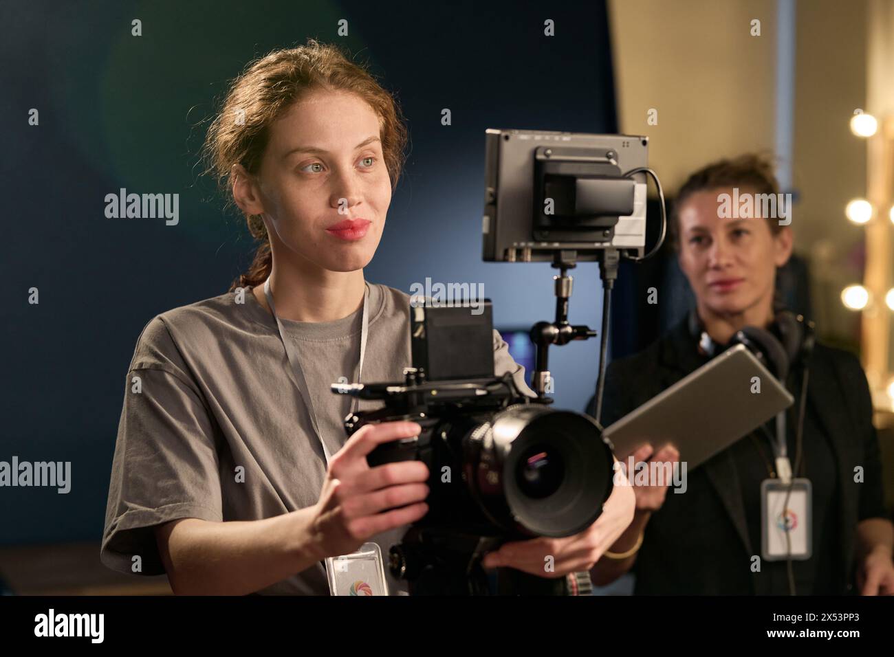 Portrait de taille haute de jeune femme souriante exploitant un équipement de caméra professionnel sur le plateau pendant l'espace de copie de production vidéo Banque D'Images
