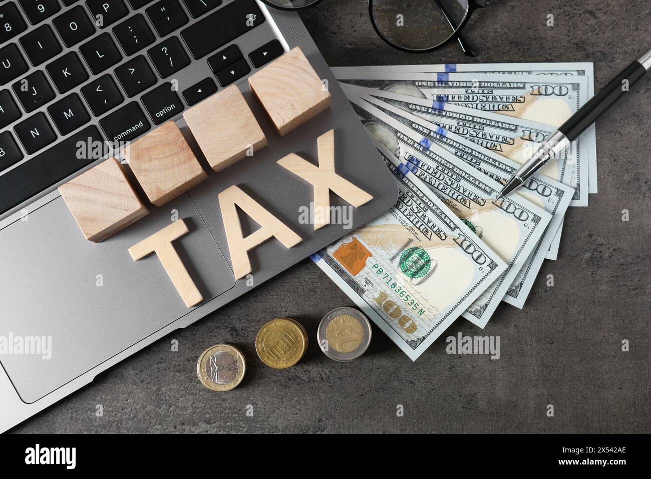 Word Tax fait de lettres en bois, cubes, ordinateur portable, billets de banque et pièces de monnaie sur la table grise, pose à plat Banque D'Images