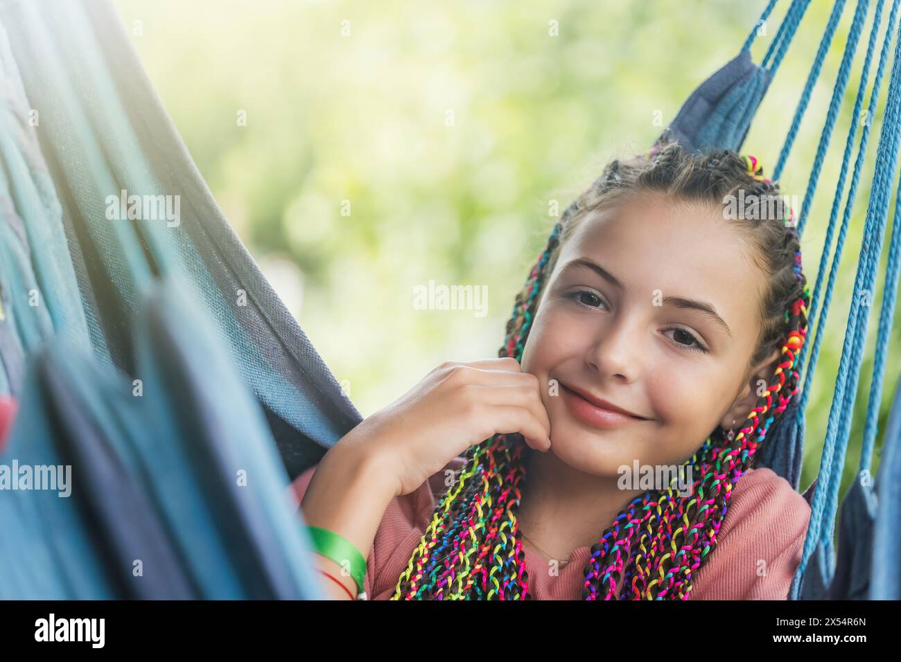 Gros plan portrait de jeune fille souriante avec des tresses colorées dans ses cheveux posant sur un hamac bleu. Horizontalement. Banque D'Images
