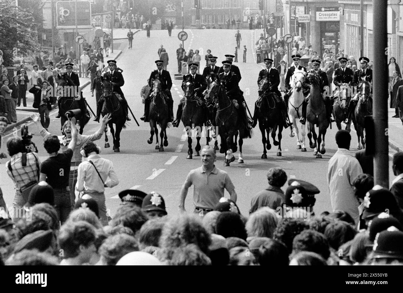 Jouer pour les caméras qu'un démonstrateur obtiennent sur le chemin d'une équipe de télévision filmant. Lewisham Londres 1970s Royaume-Uni. La police montée se dirige vers la foule de manifestants de gauche qui protestent contre le Front national, traversant New Cross jusqu'à Lewisham. New Cross, Londres, Angleterre 13 août 1977. HOMER SYKES. Banque D'Images