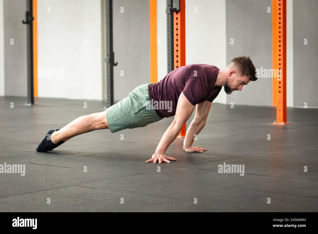 Vue latérale complète du corps d'un homme adulte barbu fort en vêtements de sport regardant vers le bas tout en étant allongé sur le sol de gymnastique faisant de l'exercice maigre de planche calisthenics en plein jour Banque D'Images