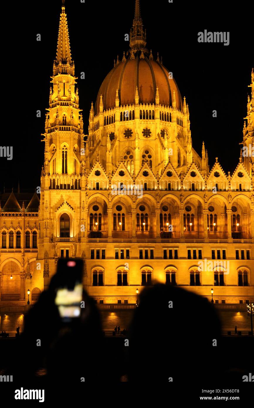 Un touriste tente de capturer avec son téléphone la vue nocturne du bâtiment illuminé du Parlement hongrois, à Budapest. Banque D'Images