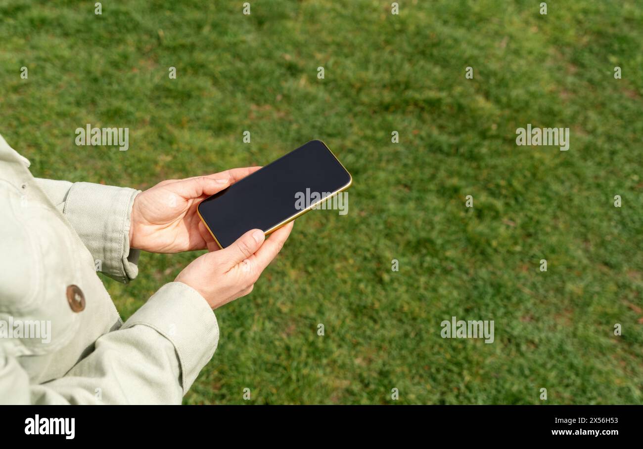 Téléphone à écran tactile dans les mains de la femme au-dessus de la pelouse verte. Banque D'Images