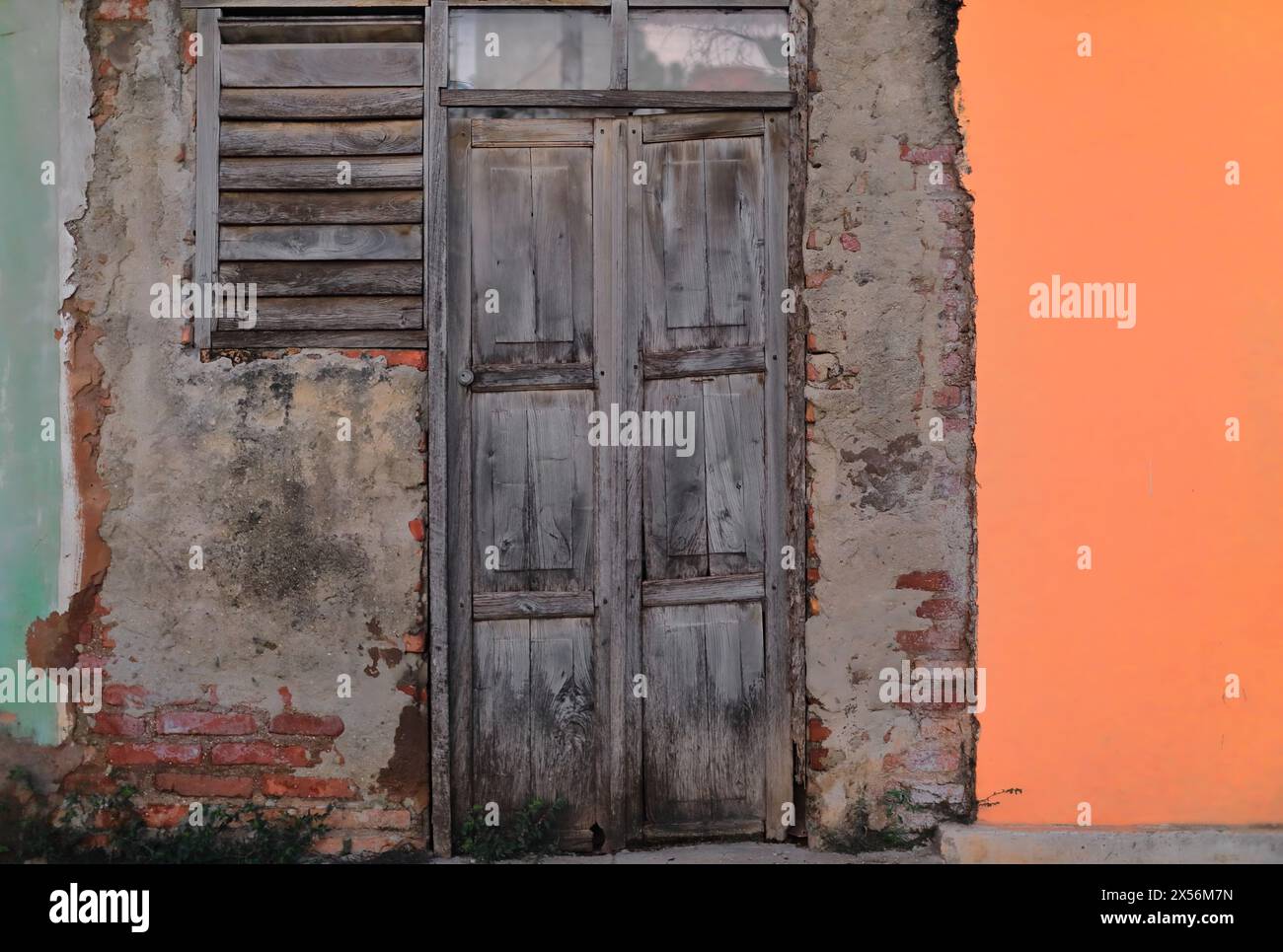 251 porte en bois totalement délavé sur un mur de briques ébréché et non rendu entre d'autres façades vertes et oranges, dans le quartier Plaza Mayor Square. Trinidad-Cuba. Banque D'Images