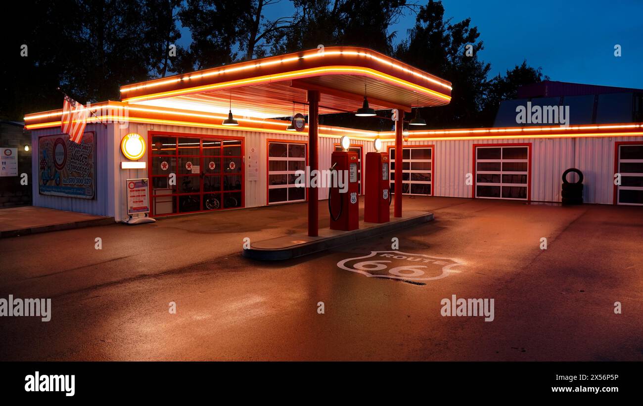 Ancienne station-service magnifiquement éclairée par une nuit pluvieuse avec reflet sur le sol mouillé Banque D'Images