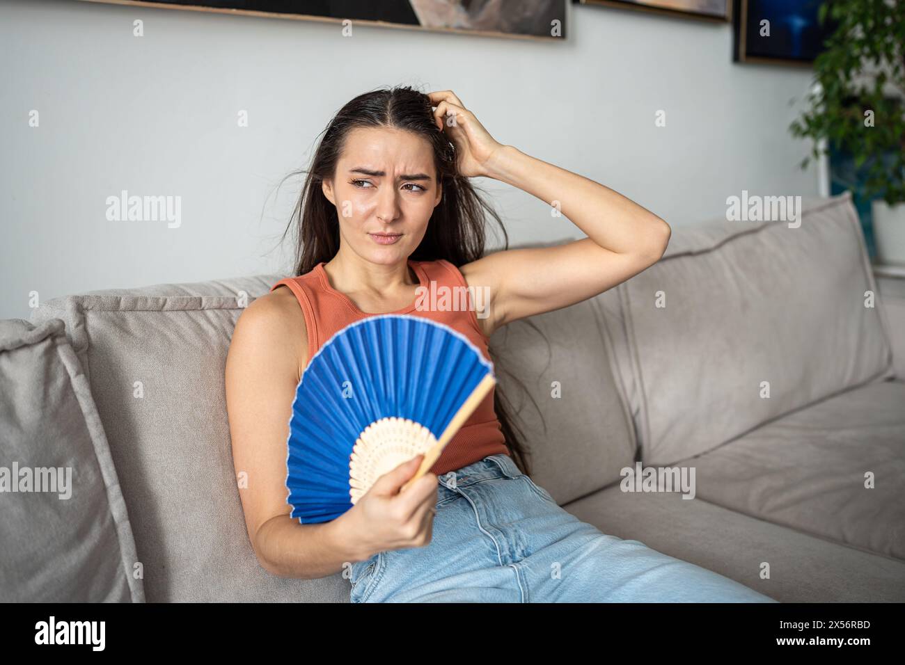 Femme avec une expression inconfortable sur le visage essayant de faire face à la chaleur terrible de l'été en utilisant un ventilateur Banque D'Images