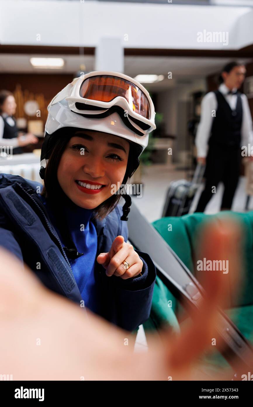 Jeune femme asiatique à la station de ski exclusive tenant un téléphone portable pour photo selfie. Voyageuse passionnée portant une veste d'hiver, des lunettes de ski et un casque prêt pour les activités de sports d'hiver. Banque D'Images