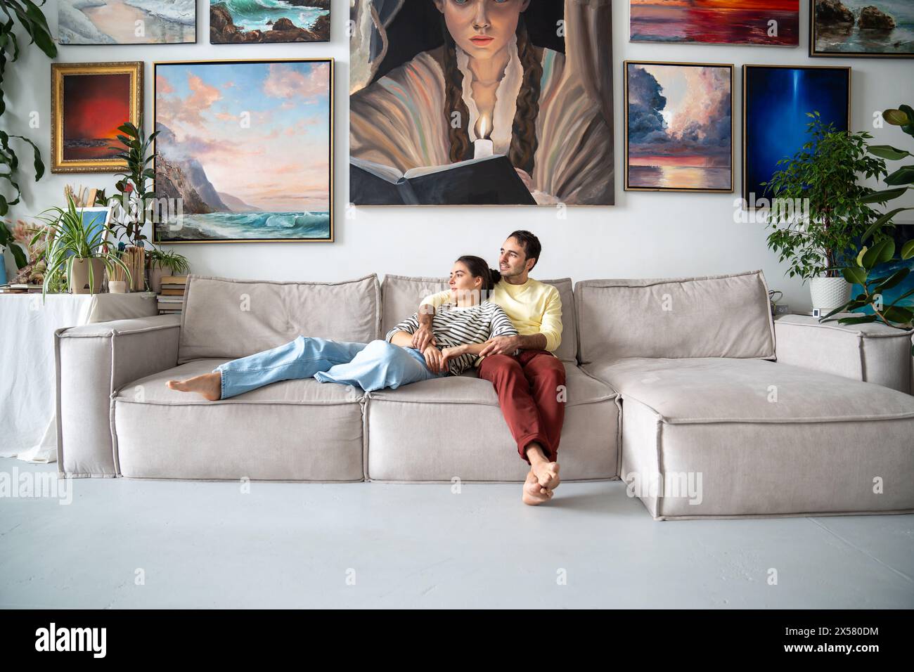 Couples calmes peintres se reposant dans le home studio. Heureux gars détendu, filles artistes câlins sur le canapé Banque D'Images