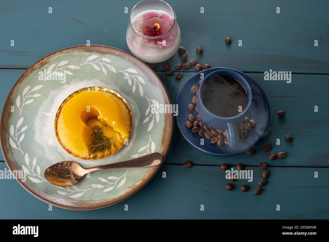 Petit quindim, sucré traditionnel brésilien, à côté d'une cuillère, tasse à café et une bougie 10. Banque D'Images