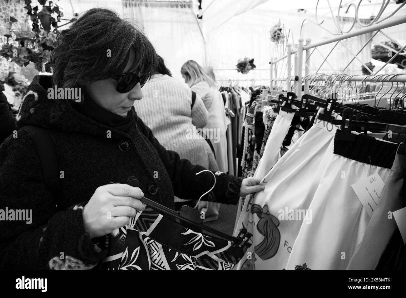 Scène de vie urbaine : femme sélectionnant des vêtements de l'étal de marché extérieur Banque D'Images