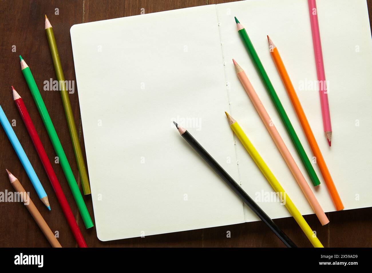 Onze crayons de couleur et un carnet de croquis vide sur une table en bois Banque D'Images