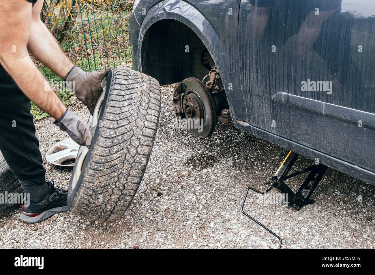 Propriétaire de voiture changeant un pneu crevé à l'extérieur dans la rue. Déposer et maintenir le pneu et le cric a soulevé la voiture. Banque D'Images