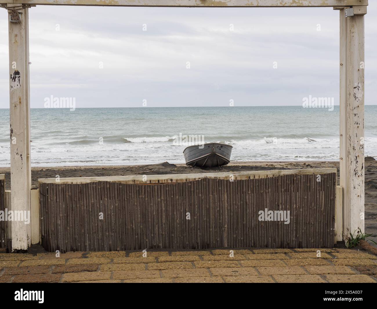 Mer d'hiver : sur la plage, la structure d'un kiosque en bois encadre un petit bateau couché sur le rivage. Mer Tyrrhénienne, côte du Latium, Italie. Banque D'Images