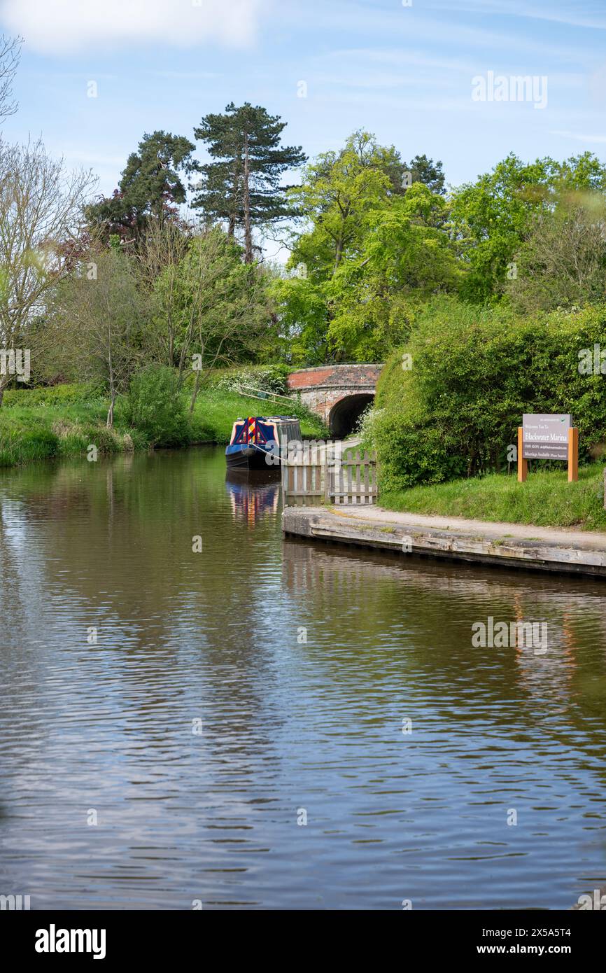 Un bateau étroit amarré près de l'entrée d'une marina près d'Ellesmere dans le Shropshire entouré d'arbres et de buissons. Banque D'Images