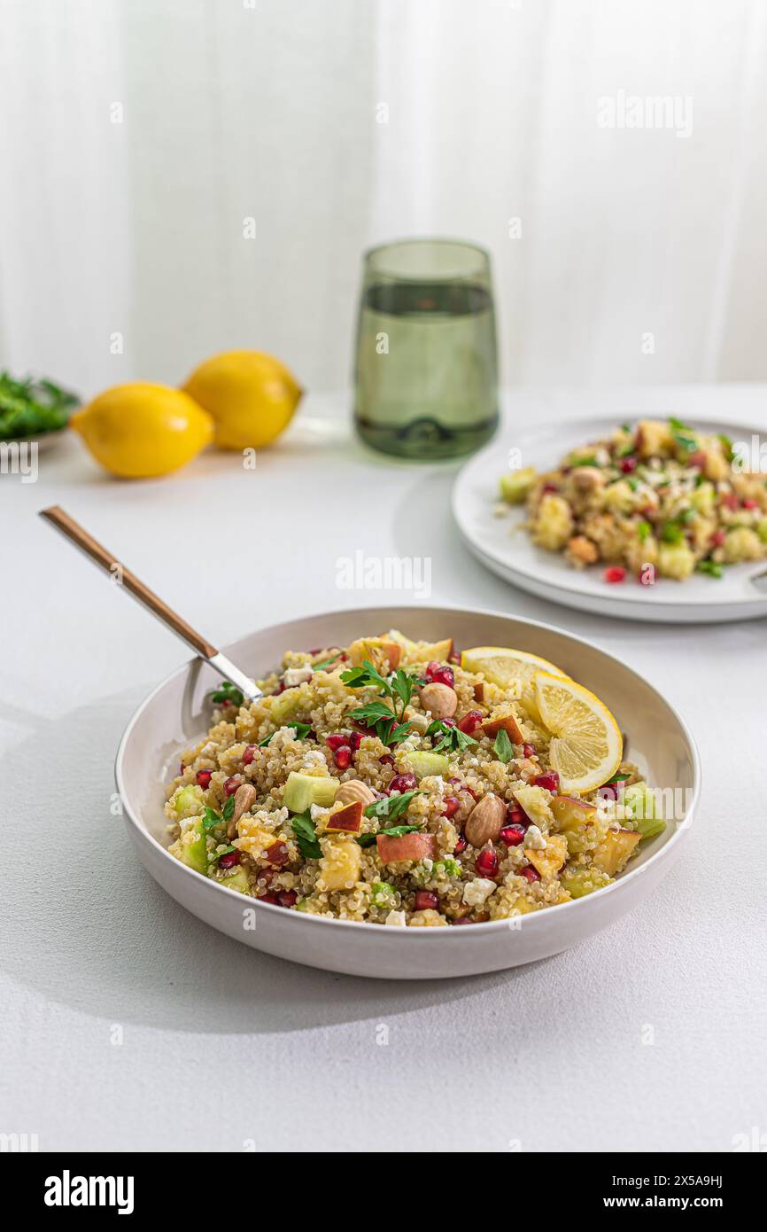 Une salade de quinoa vibrante mélangée avec des épices au curry, des légumes frais, des noix et des tranches de citron, présentée dans un bol sur une table blanche, avec un doux rétro-éclairage Banque D'Images