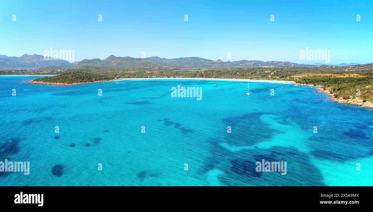 Une vue panoramique sur la magnifique côte de la plage de Brandinchi, Sardaigne, Italie, avec des eaux turquoises, voiliers, et un ciel bleu clair Banque D'Images