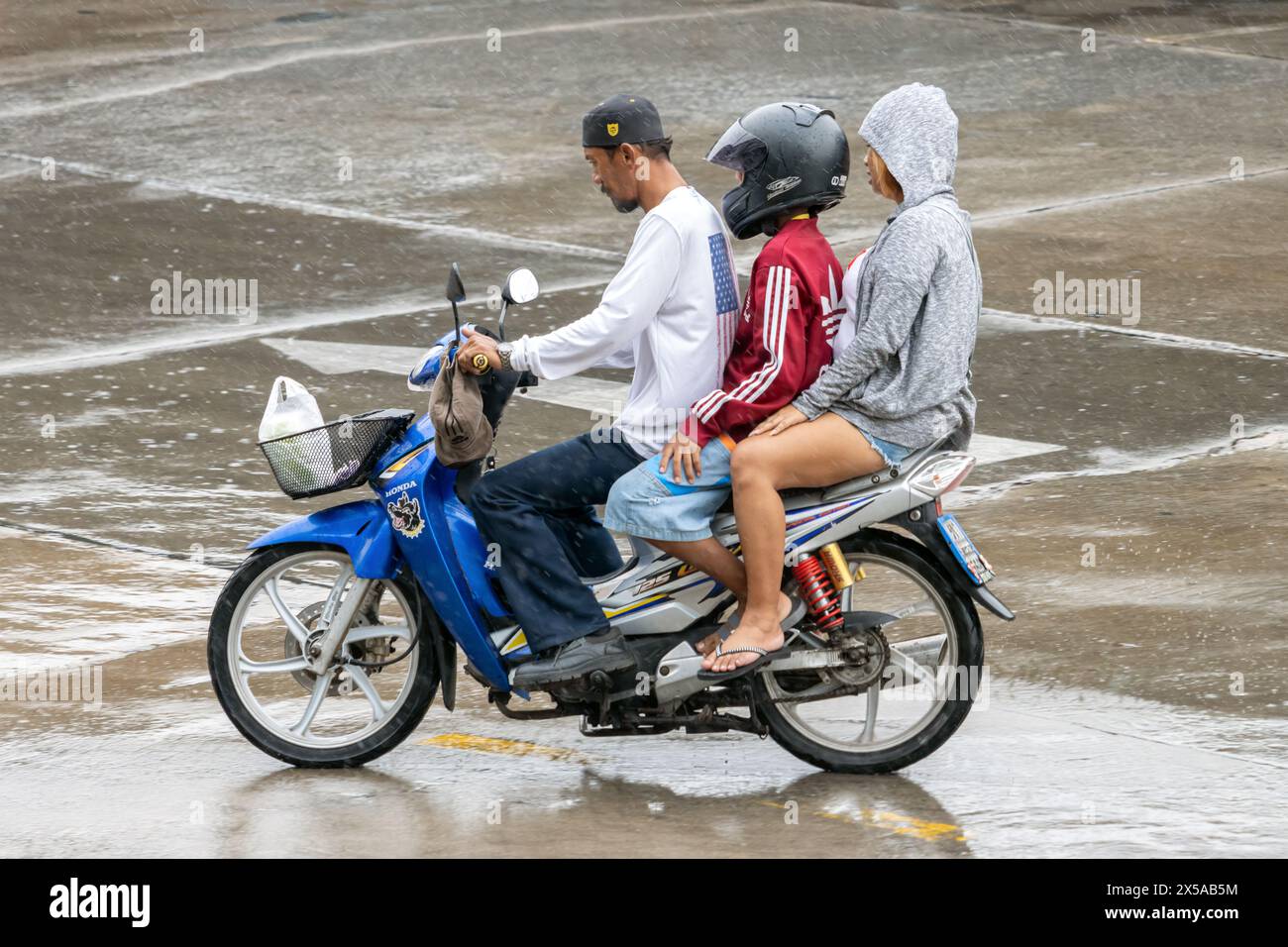 SAMUT PRAKAN, THAÏLANDE, 20 mars 2024, le trio conduit une moto ensemble sous la pluie Banque D'Images
