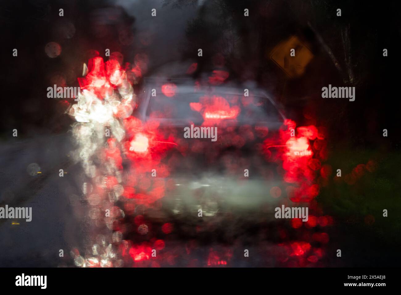 Image abstraite de phares blancs et de feux arrière de voiture rouges vus à travers un pare-brise humide sur un après-midi pluvieux. Banque D'Images