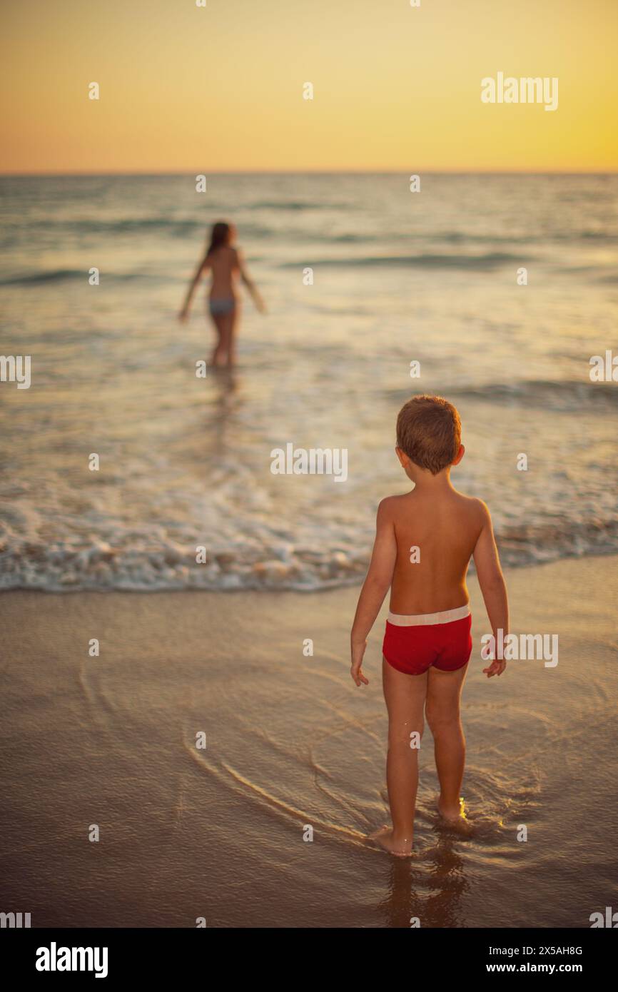Deux jeunes enfants profitent de la mer au crépuscule sur une plage de sable dans la province de Cadix, en Espagne. Banque D'Images