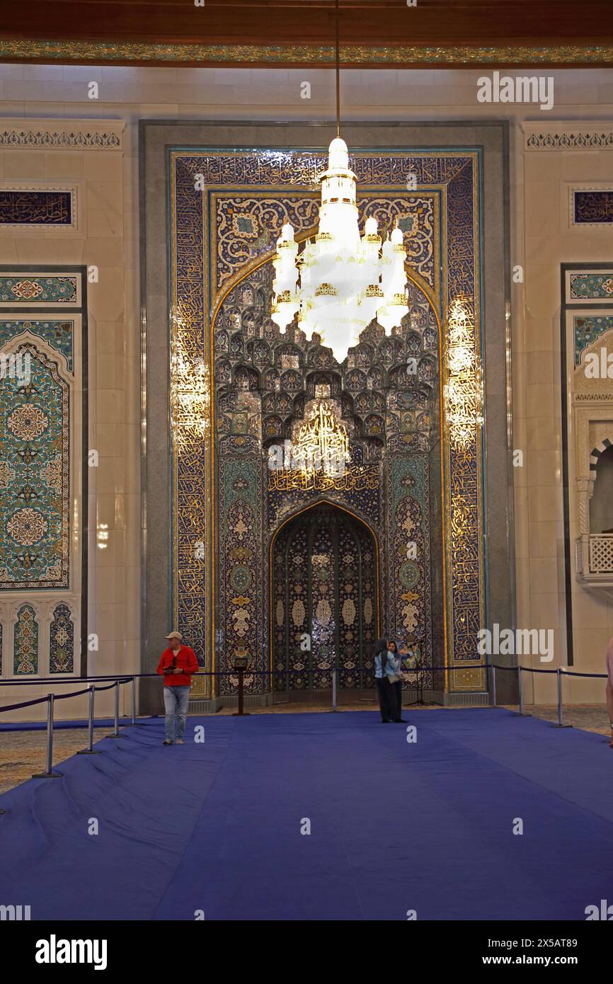 Sultan Qaboos Grand Mosquée touristes intérieurs debout sur le tapis bleu protecteur par le mihrab Muscat Oman Banque D'Images