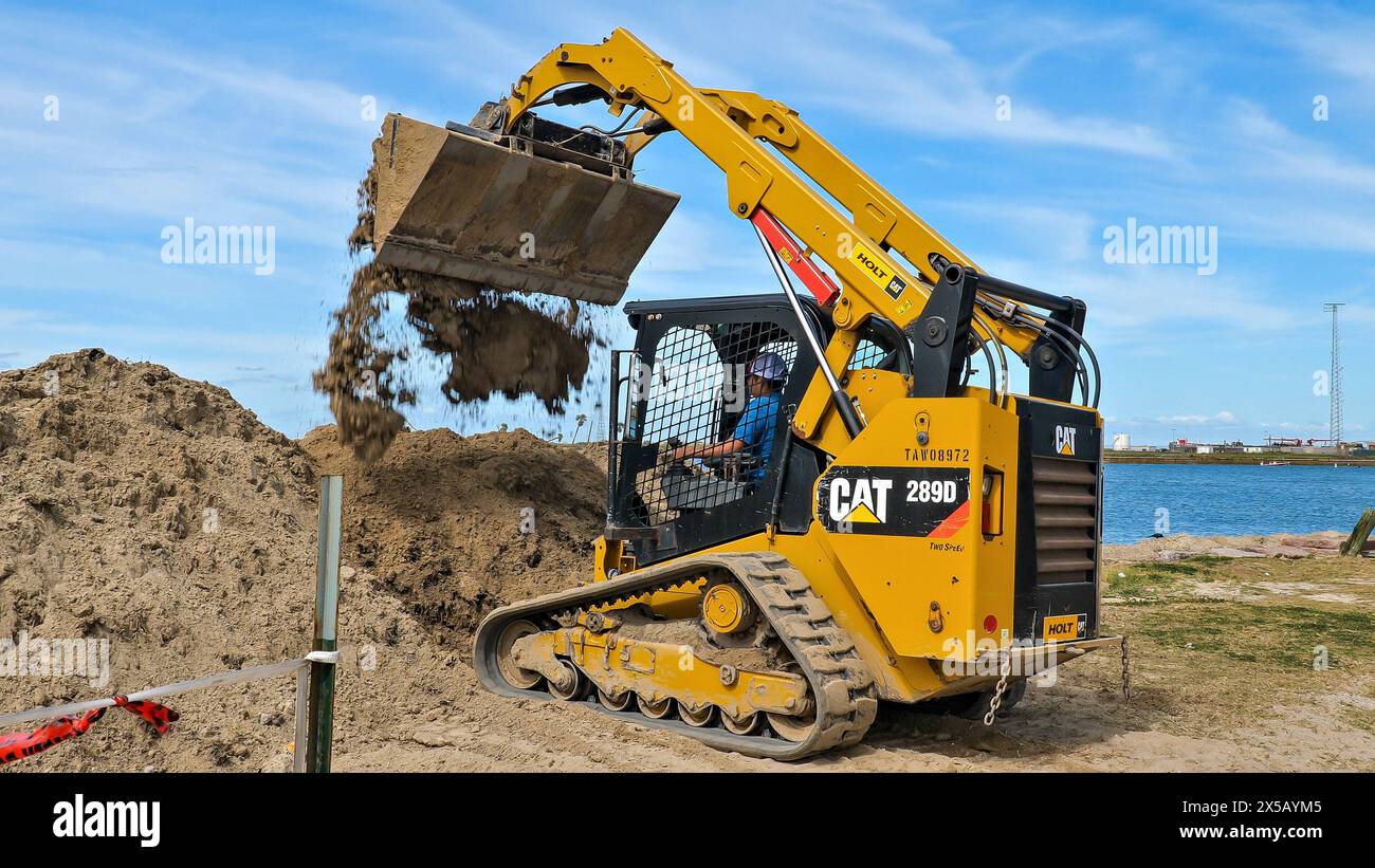 PORT ARANSAS, TX - 29 février 2020 : un ouvrier conduit une chargeuse frontale CAT 289D jaune pour vider une charge de saleté sur un chantier de construction près de l'ELAT Banque D'Images