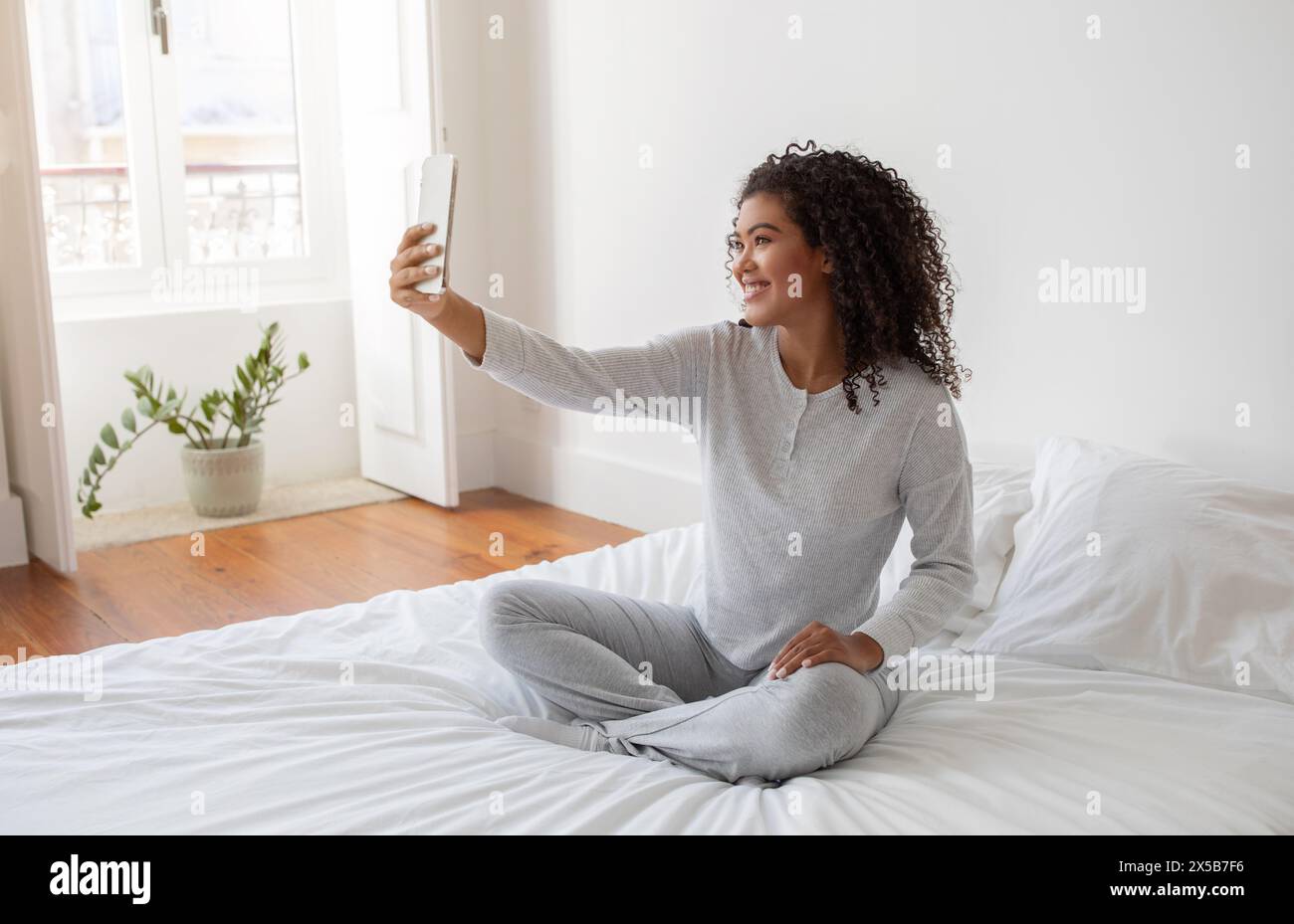 Femme assise sur le lit prenant Selfie après le réveil Banque D'Images