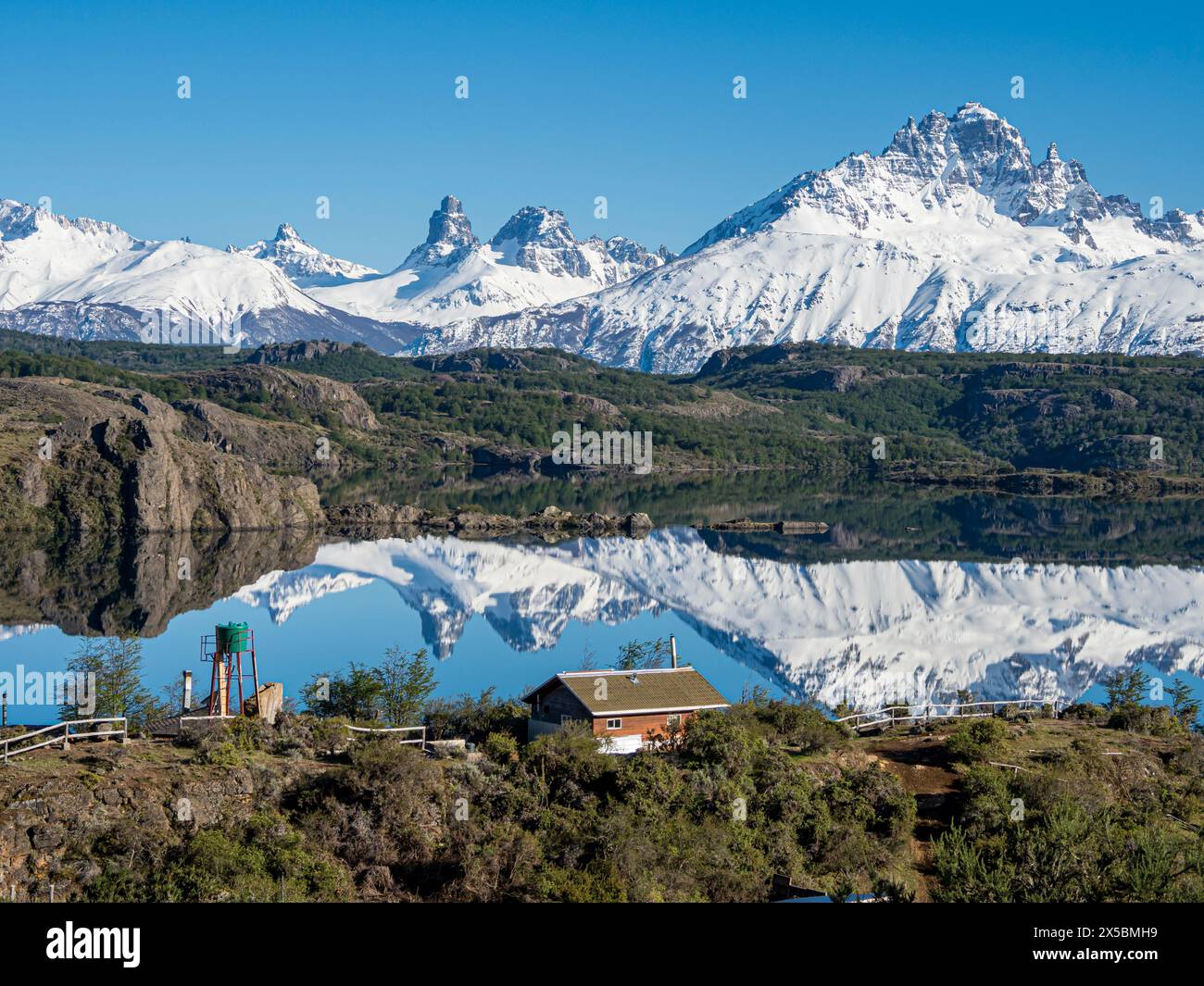 Le mont enneigé Cerro Castillo se reflète dans un lac, petite ferme au bord du lac, Patagonie, Chili Banque D'Images