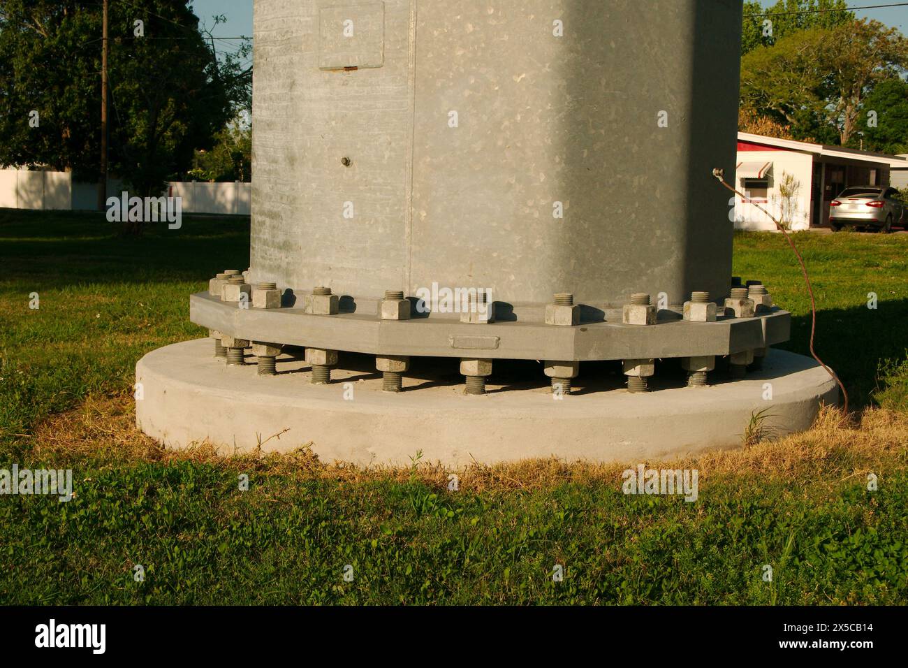 Gros plan au-dessus de l'herbe verte bas large horizontal d'une base de poteau de service en acier vis avec boulons et écrous de base en béton. Près du coucher du soleil par une journée ensoleillée Banque D'Images