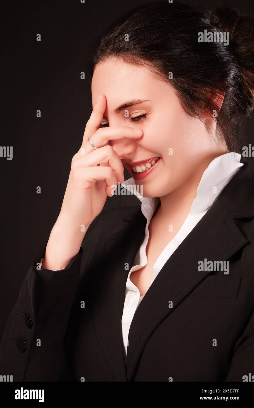 Jeune femme professionnelle dans un costume d'affaires noir rit tout en cachant ludique son visage, montrant un esprit léger Banque D'Images