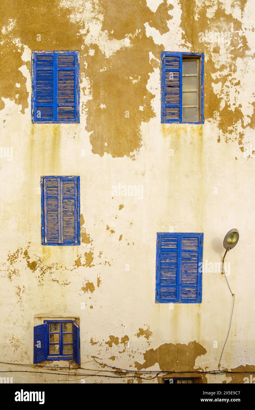 Vue sur les fenêtres bleues et les volets sur un mur de la vieille maison avec de la peinture blanche. Essaouira (Mogador), Maroc Banque D'Images