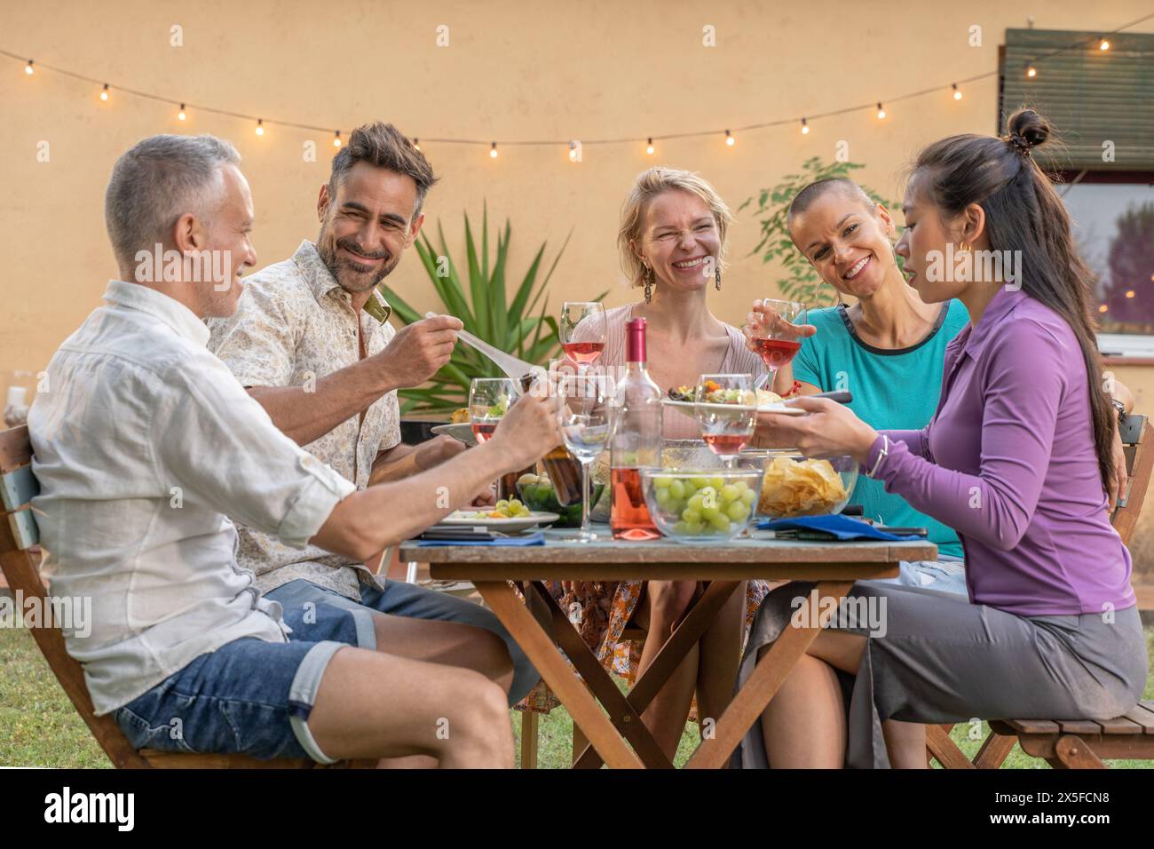 Amis mangeant et buvant heureux souriant et riant dans le patio. Des gens joyeux d'âge moyen autour de la table pendant les vacances d'été. Banque D'Images