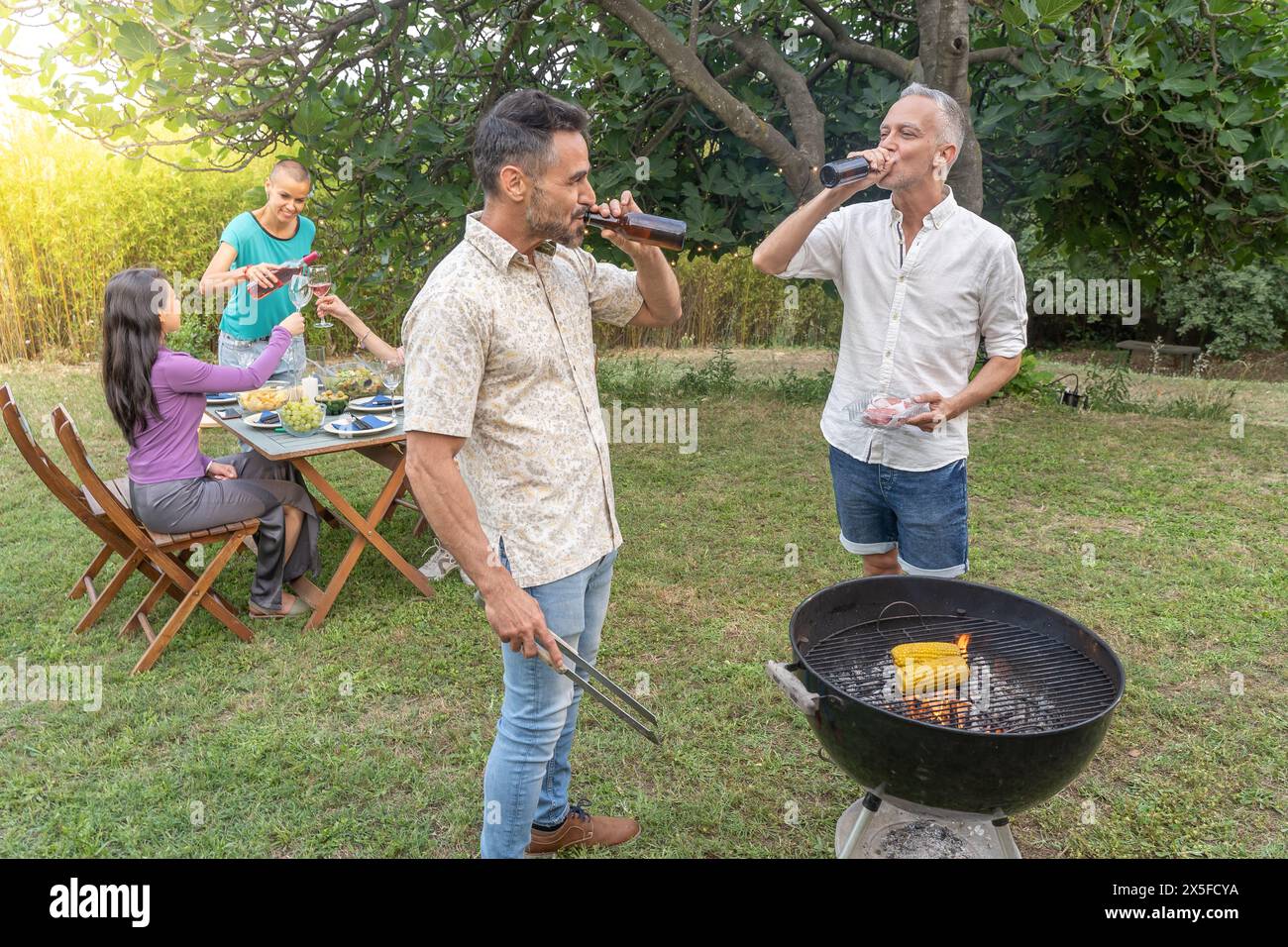 Groupe d'amis buvant autour du barbecue. Les gens souriants cuisinent sur le patio. Banque D'Images