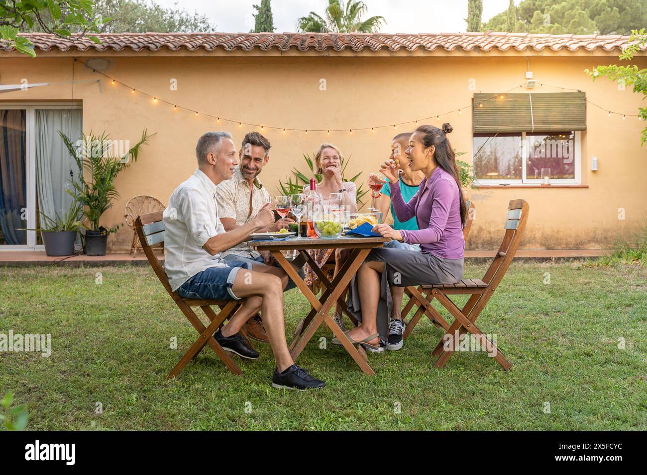 Groupe d'amis multiethniques mangeant et buvant heureux souriant et riant dans le patio. Des gens joyeux d'âge moyen autour de la table. Banque D'Images