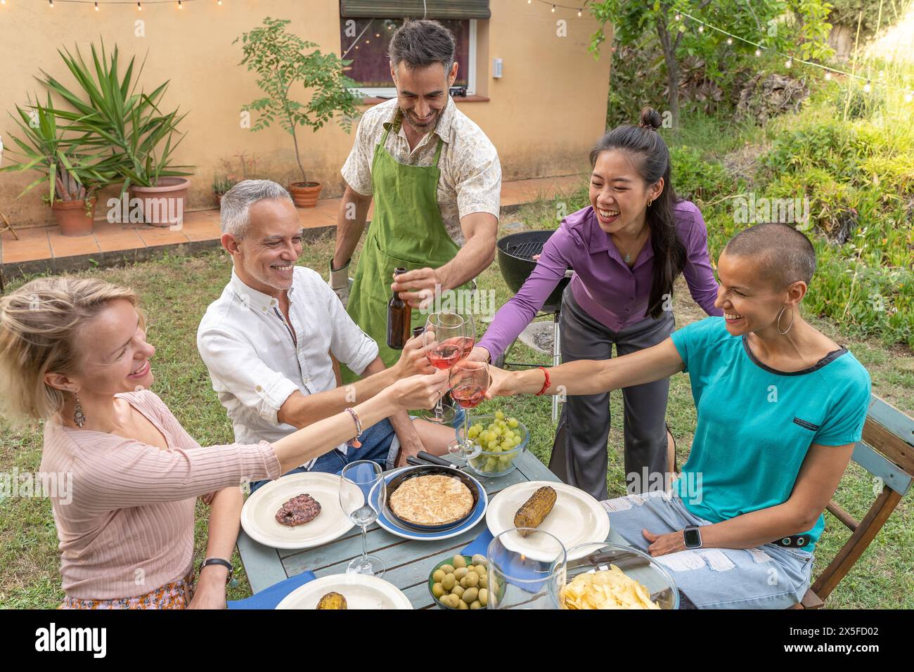 Toast familial multiracial avec grand sourire autour de la table au restaurant patio de la maison. Banque D'Images