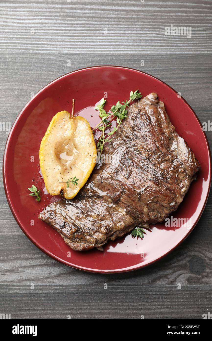 Délicieuse viande de bœuf rôtie, poire caramélisée et thym sur table en bois gris, vue de dessus Banque D'Images